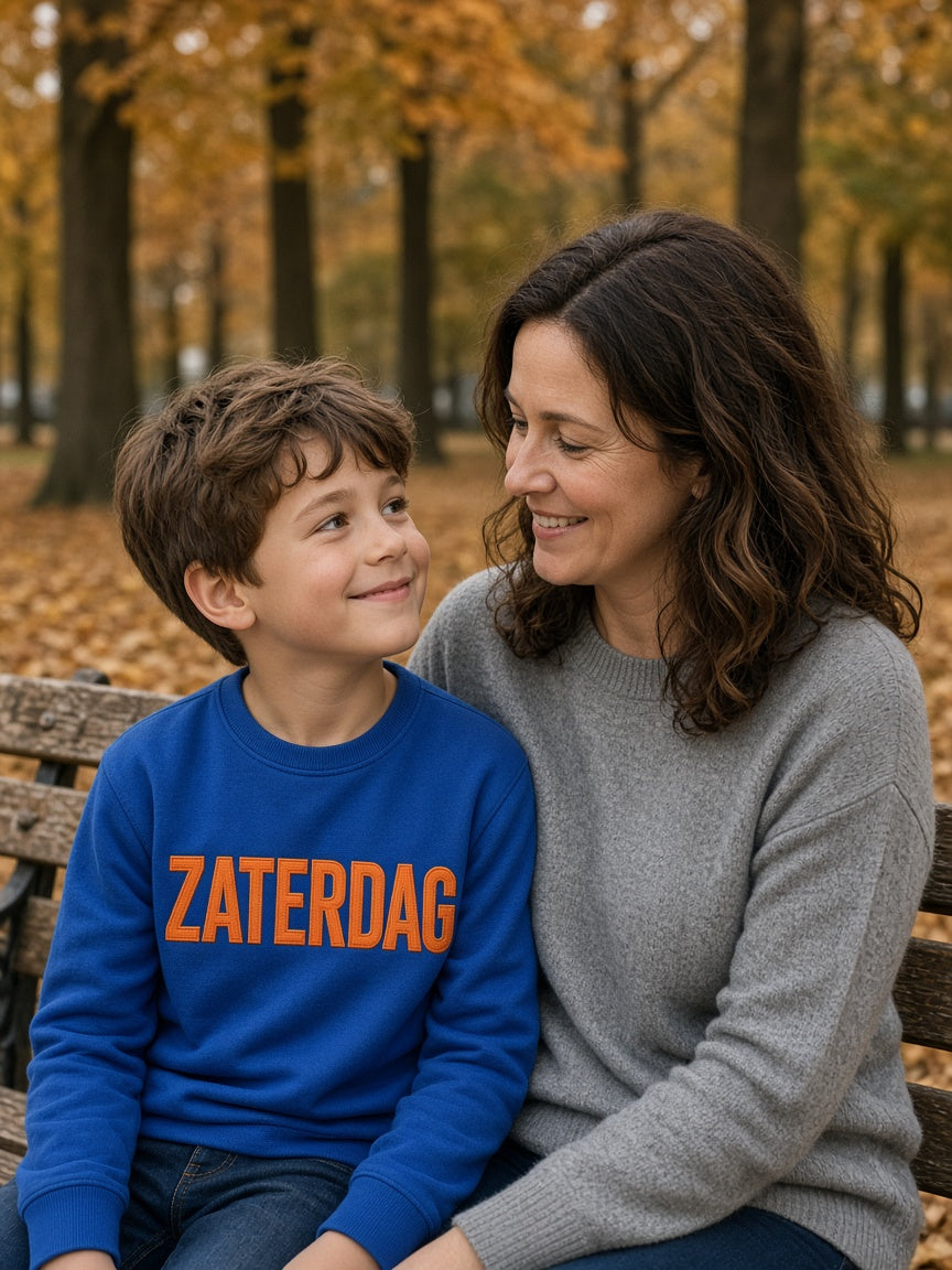 Kind in royal blauwe kindertrui met eigen woord ZATERDAG in oranje garen, met moeder