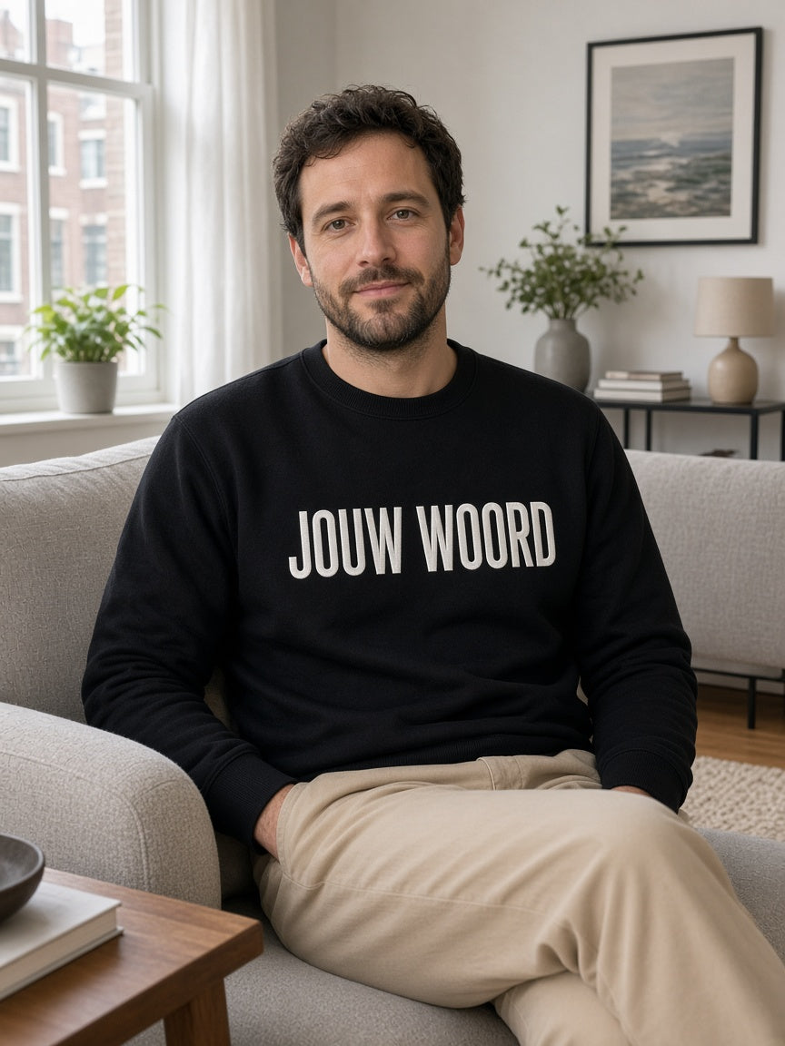 Man in zwarte EIGEN WOORD sweater met JOUW WOORD geborduurd in wit (heren)
