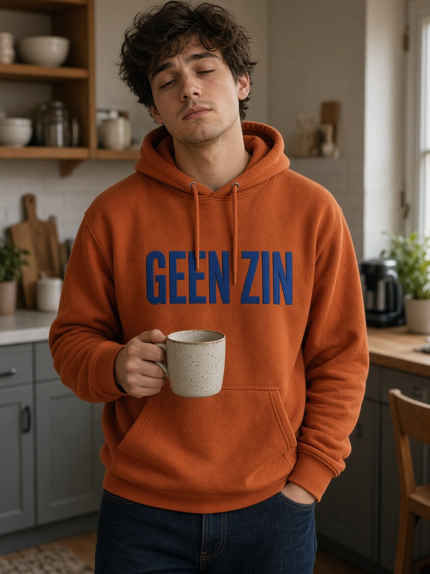 Man draagt de HUMEURIG GEEN ZIN Hoodie in oranje met royal blauw borduursel (heren)
