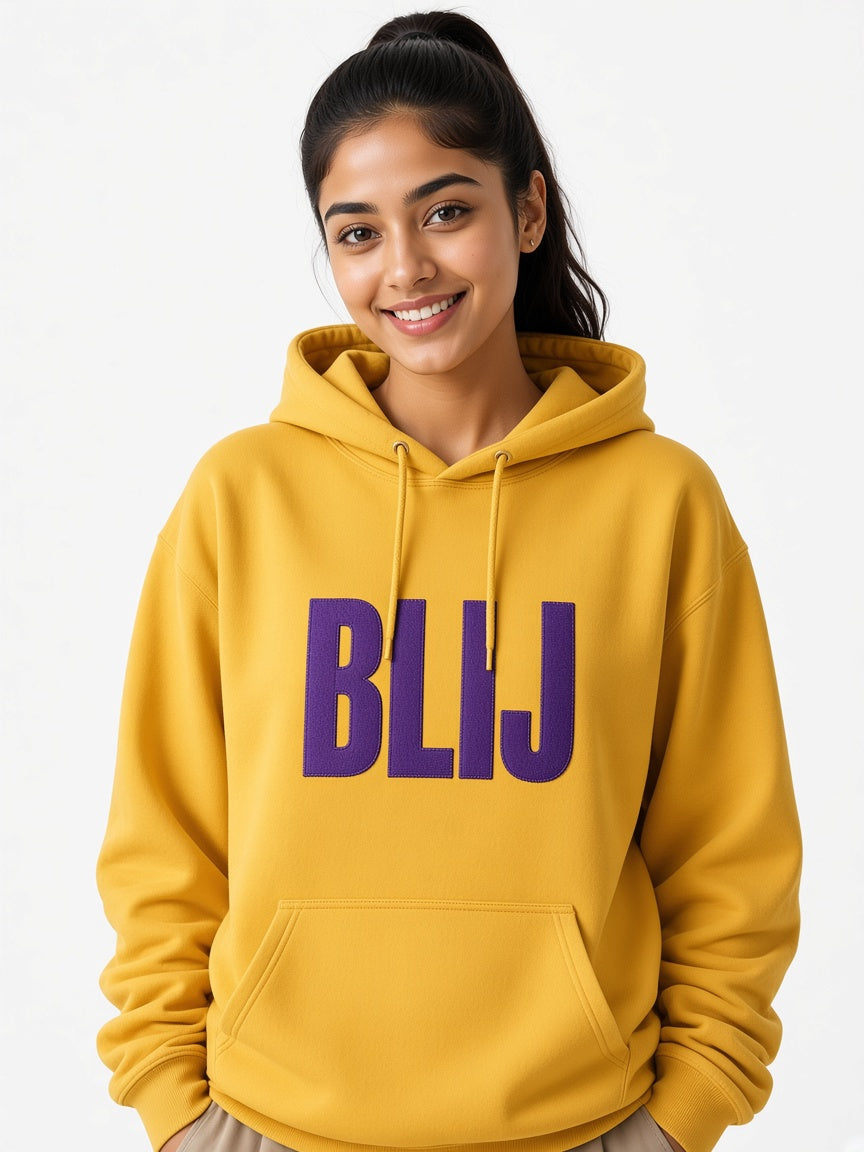 Model draagt de HUMEURIG BLIJ Hoodie in Goud/Paars met het woord BLIJ geborduurd (dames)