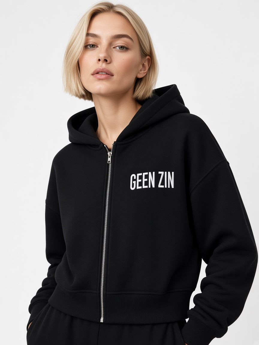 Model draagt de HUMEURIG GEEN ZIN Zip Hoodie in Zwart met het woord GEEN ZIN geborduurd