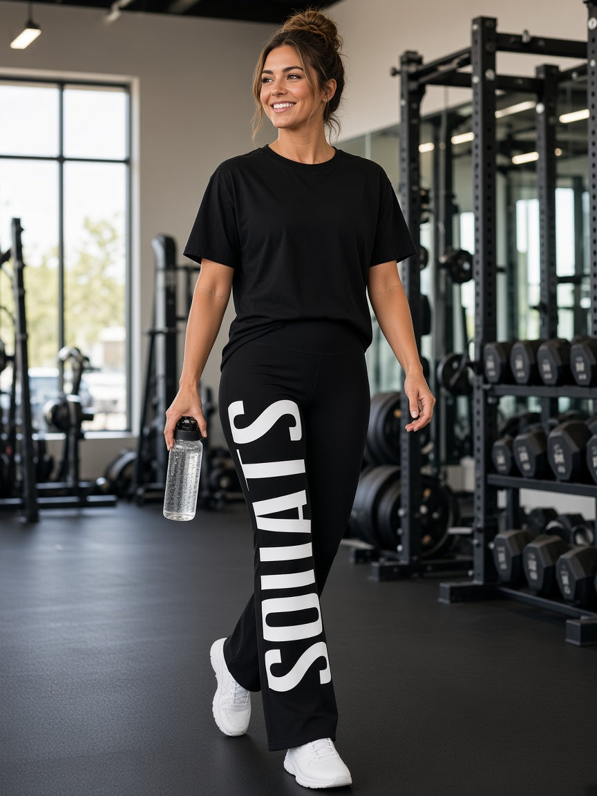 Model draagt de HUMEURIG SQUATS Flare Legging in Zwart met het woord SQUATS all-over geprint